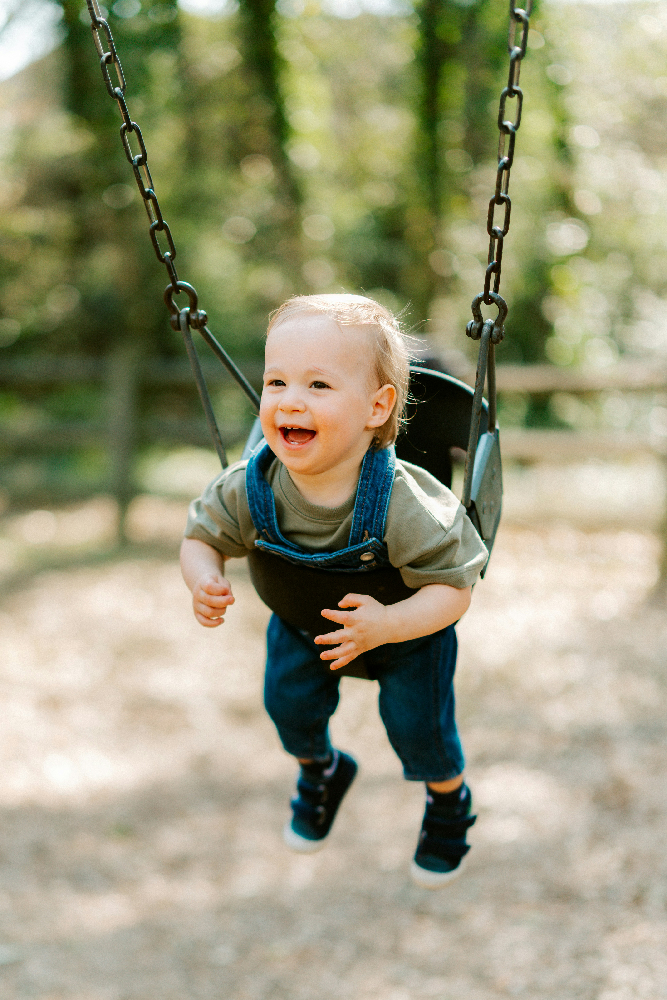 Toddler enjoying a commercial bucket swing seat with leg openings designed for young children and early playground use.
